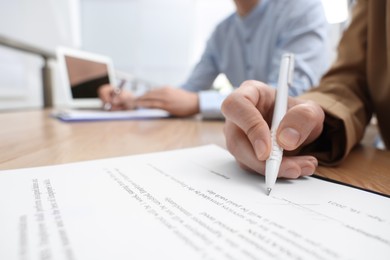 Woman signing contract at table in office, closeup.