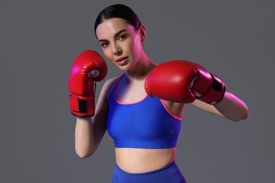 Photo of Portrait of beautiful woman wearing boxing gloves in color lights on grey background
