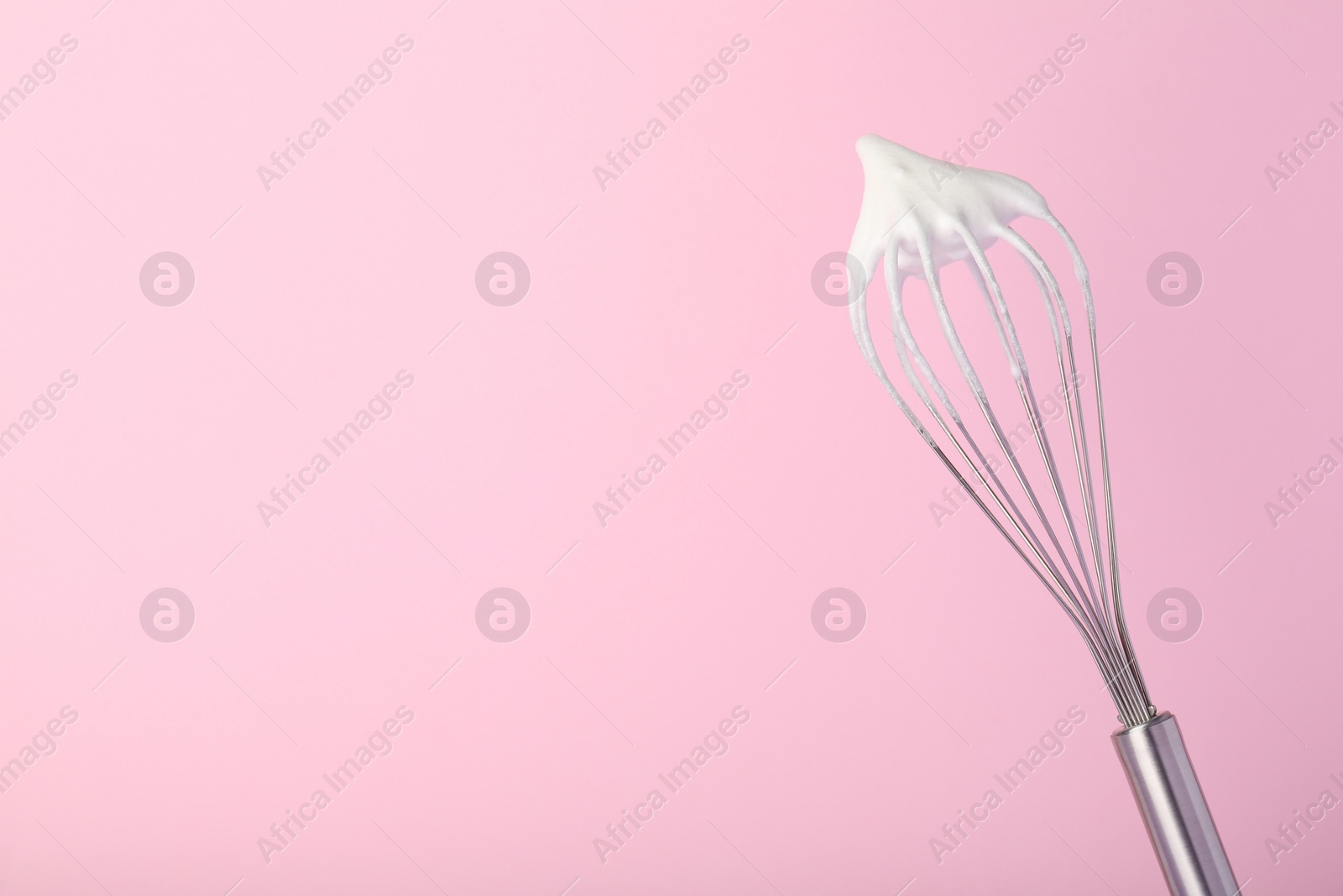 Photo of Whisk with whipped egg whites on pink background, space for text