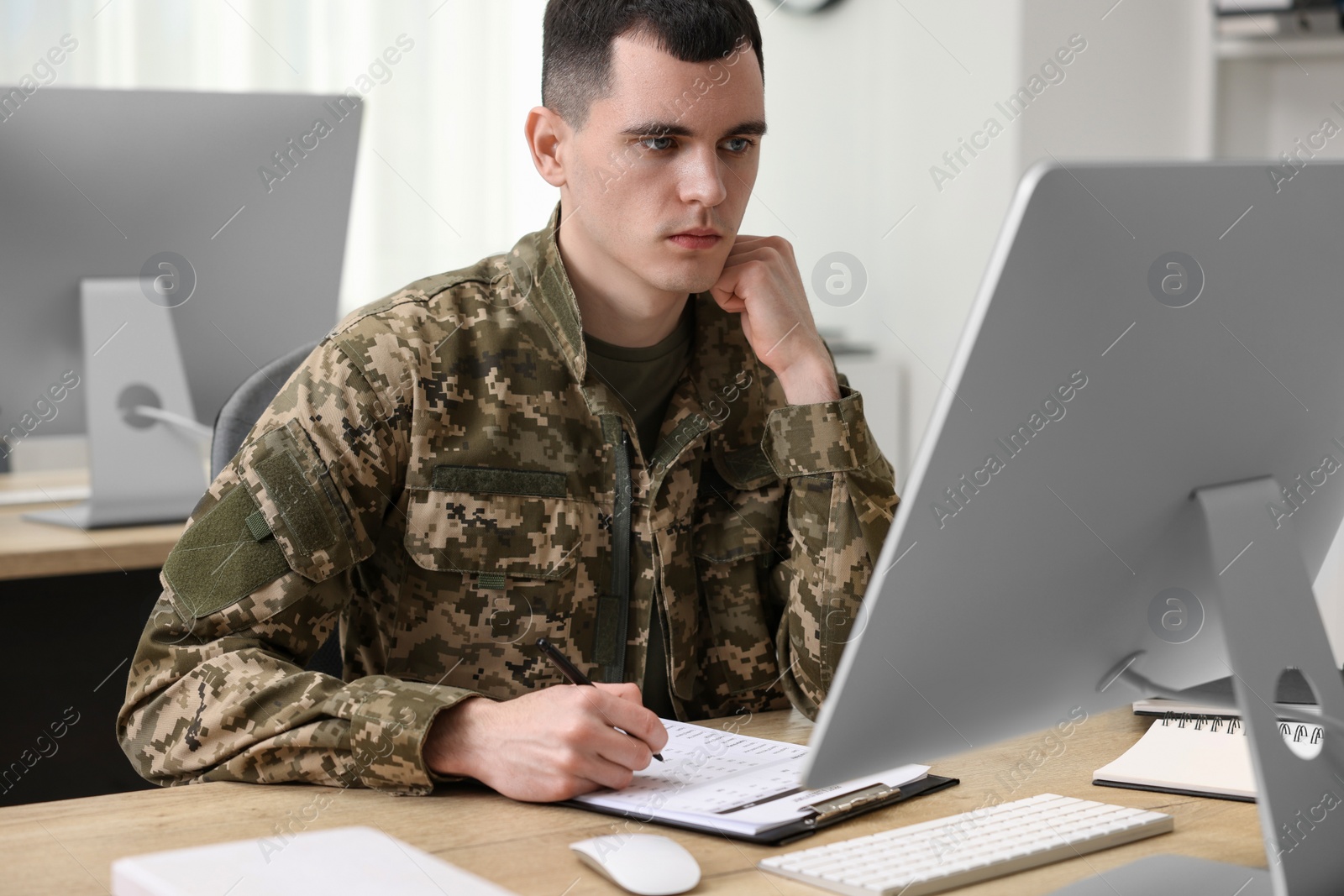 Photo of Military service. Young soldier working at wooden table in office