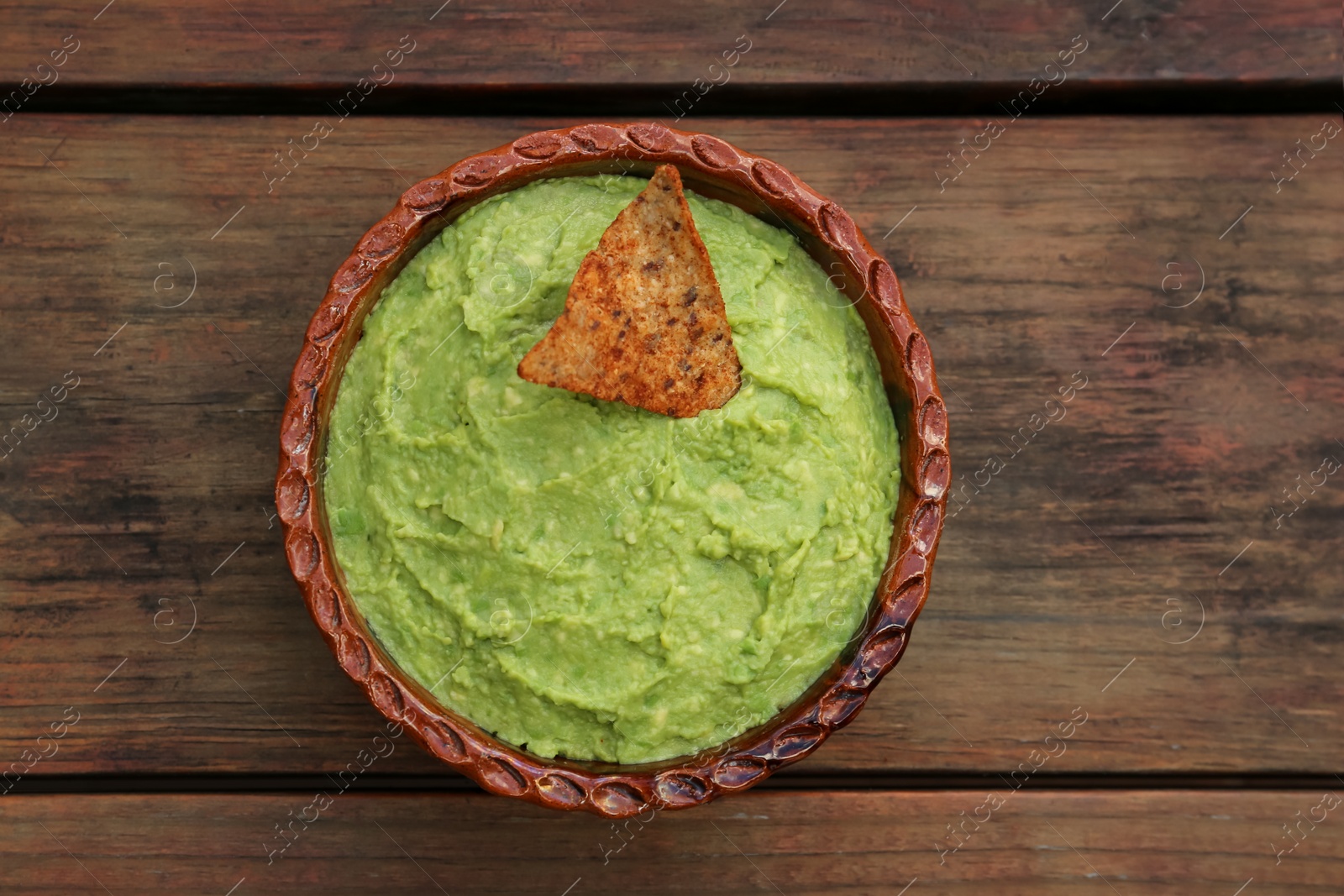 Photo of Delicious guacamole made of avocados and nachos on wooden table, top view