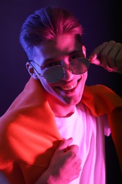 Photo of Stylish young man in sunglasses on dark background in neon lights