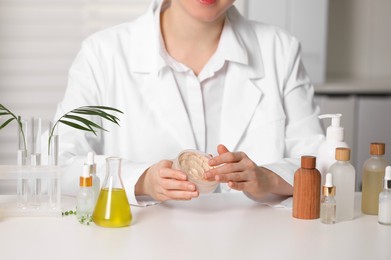 Photo of Dermatologist with jar testing cosmetic product at white table indoors, closeup