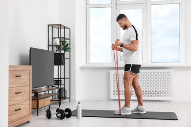 Athletic man doing exercise with elastic resistance band on mat at home