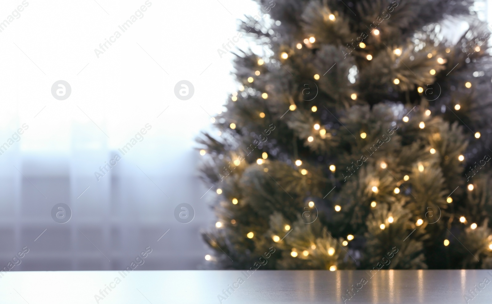 Photo of Blurred view of beautiful Christmas tree with yellow lights near window indoors, focus on table. Space for text