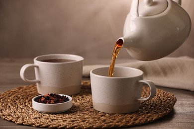 Photo of Pouring aromatic tea into cup at wooden table, closeup