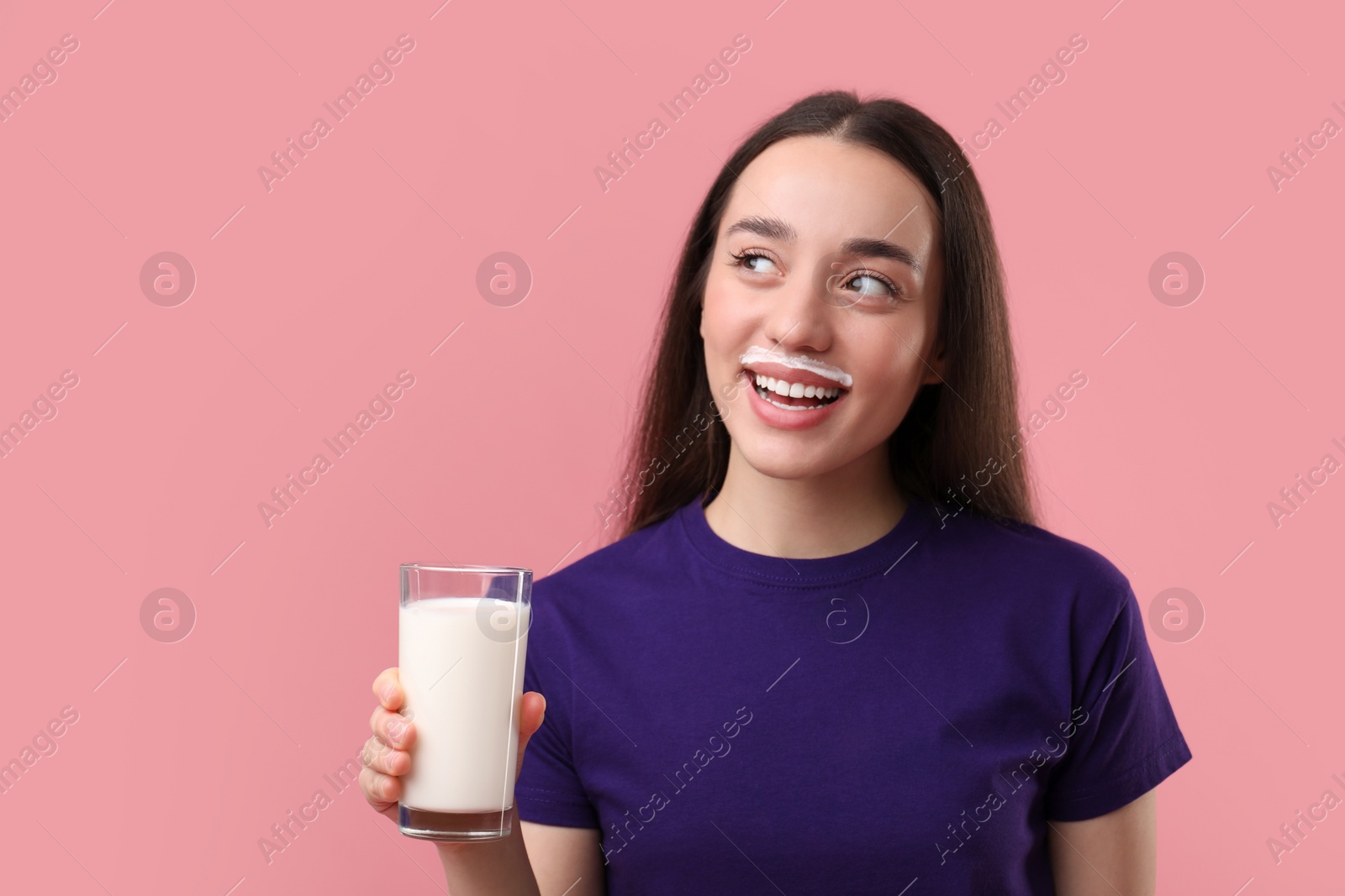 Photo of Happy woman with milk mustache holding glass of tasty dairy drink on pink background. Space for text