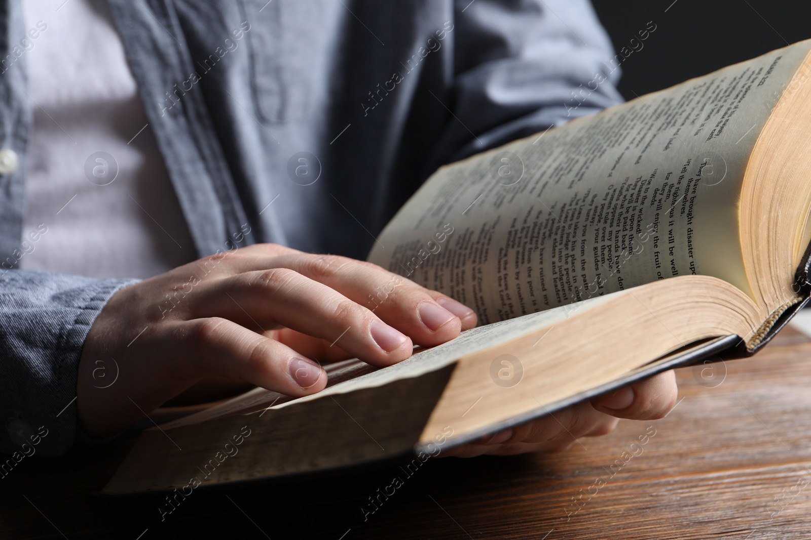 Photo of Man reading holy Bible at wooden table, closeup