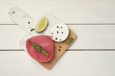 Raw tuna fillet with rosemary, lime wedge and spices on white wooden table, top view. Space for text