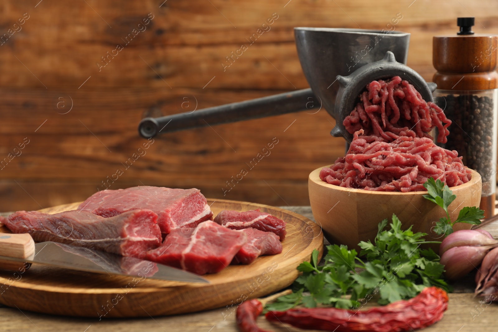 Photo of Manual meat grinder with beef, parsley and spices on wooden table