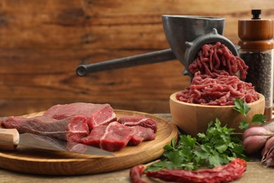 Manual meat grinder with beef, parsley and spices on wooden table