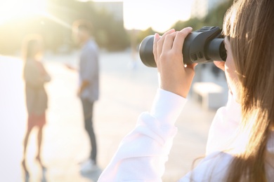Photo of Jealous ex girlfriend with binoculars spying on couple outdoors, closeup