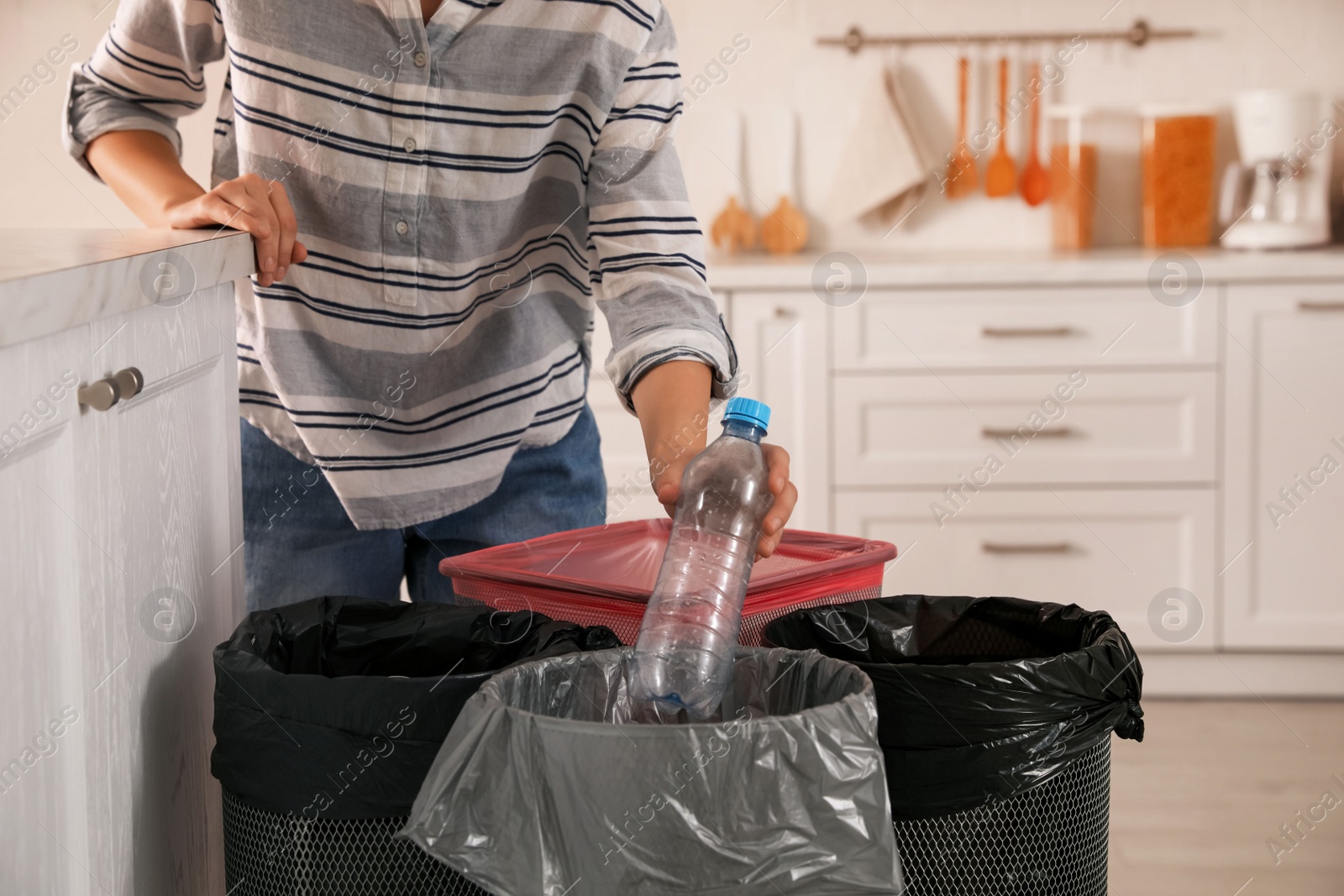 Photo of Woman throwing plastic bottle into trash bin in kitchen, closeup. Separate waste collection