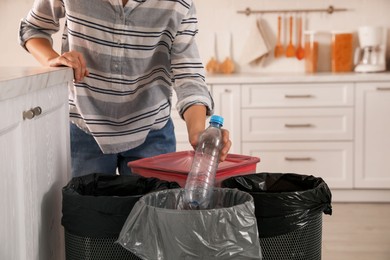 Woman throwing plastic bottle into trash bin in kitchen, closeup. Separate waste collection