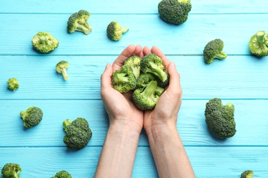 Woman holding fresh green broccoli on blue wooden table, top view