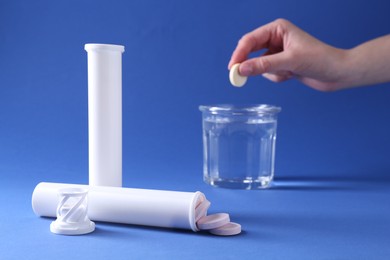 Photo of Woman putting effervescent pill into glass of water on blue background, closeup