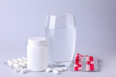 Different antidepressants, medical jar and glass of water on light grey background
