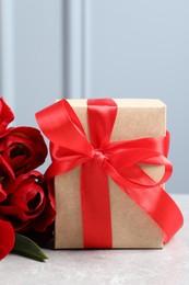 Beautiful gift box with bow and red tulip flowers on light table, closeup
