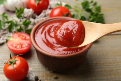 Bowl and spoon with tasty ketchup, fresh tomatoes, parsley and spices on wooden table