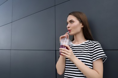 Photo of Young woman with plastic cup of fresh juice near brown wall, space for text