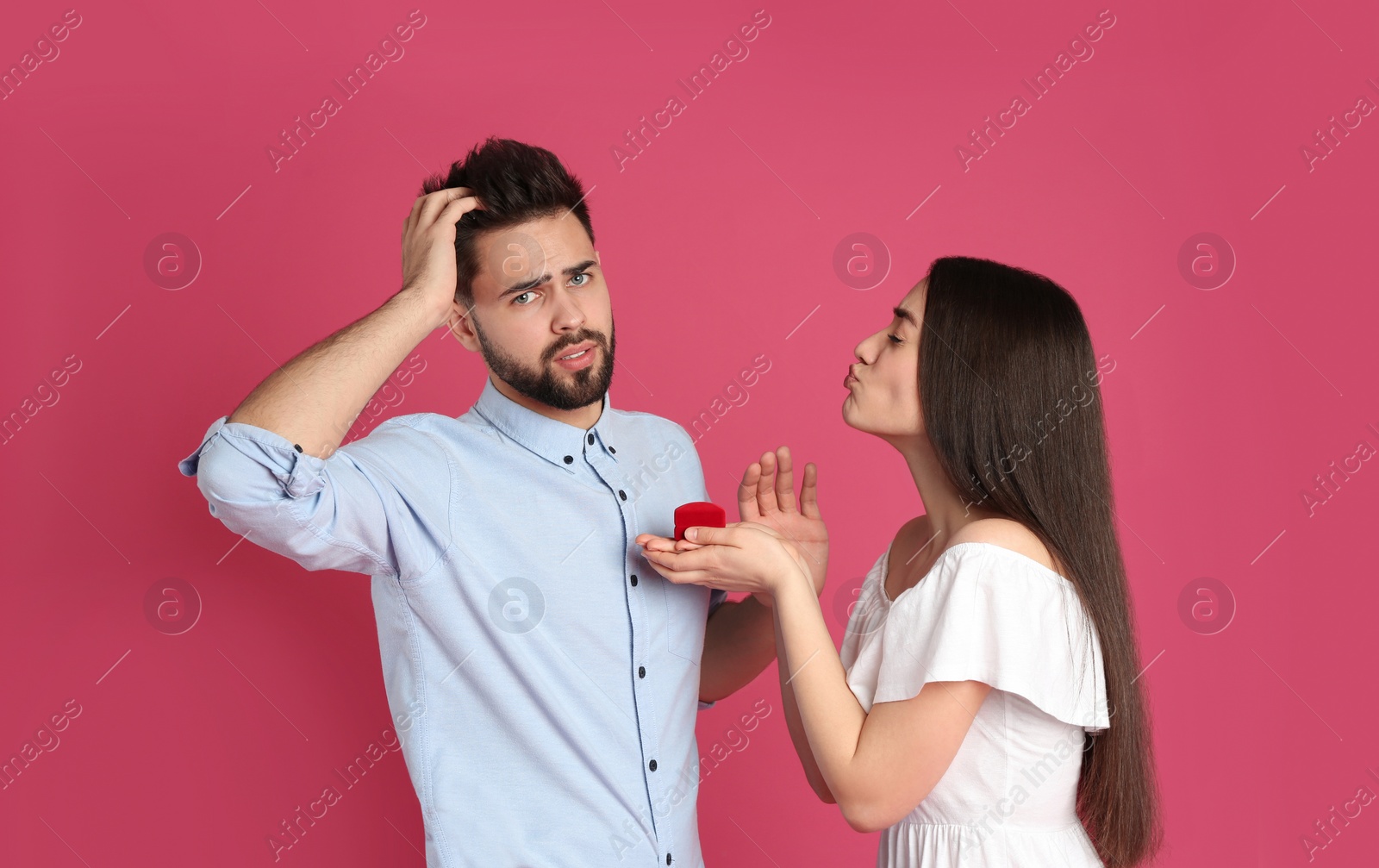 Photo of Young woman with engagement ring making marriage proposal to her boyfriend on crimson background