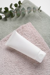 Tube of cream on towels and eucalyptus, above view