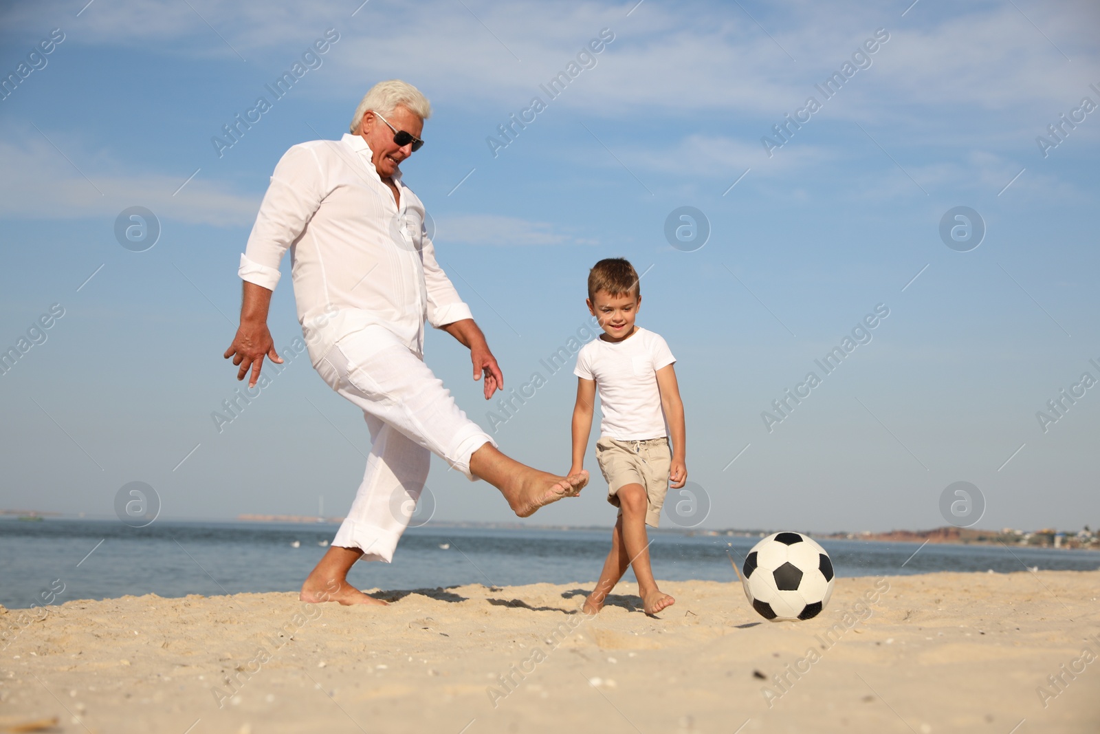 Photo of Cute little boy and grandfather playing with soccer ball on sea beach