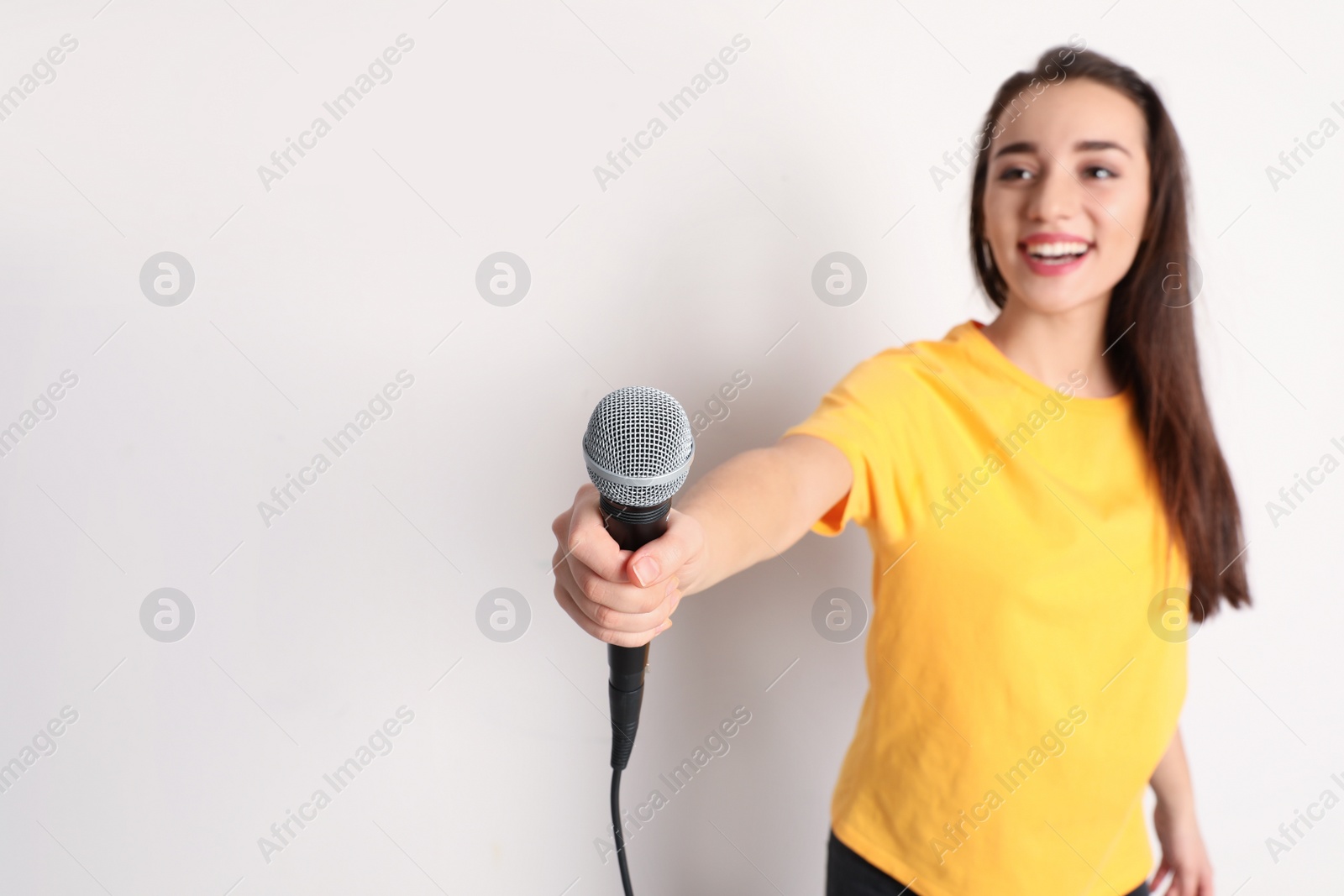 Photo of Young woman holding microphone and smiling on color background. Space for text