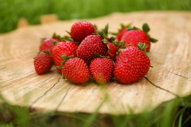 Photo of Pile of delicious ripe strawberries on tree stump outdoors, closeup