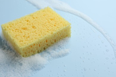 Photo of Yellow sponge with foam on light blue background, closeup