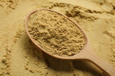 Photo of Heap of aromatic mustard powder and wooden spoon, closeup