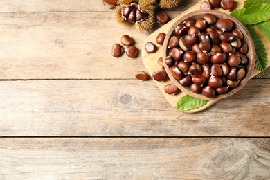 Photo of Fresh sweet edible chestnuts on wooden table, flat lay. Space for text