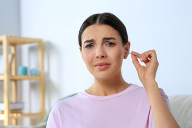 Photo of Young woman cleaning ear with cotton swab at home