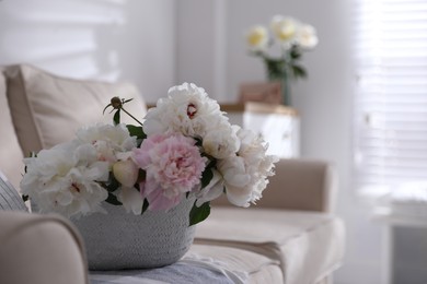 Bouquet of beautiful peony flowers in basket on sofa. Space for text