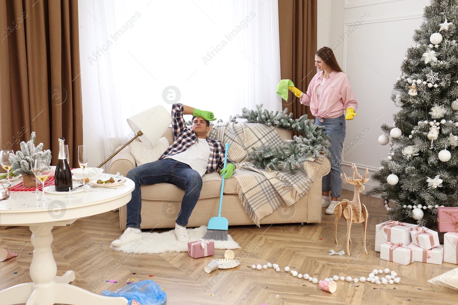 Photo of Couple quarrelling in messy room while cleaning after New Year party