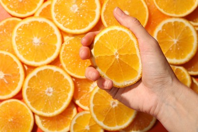 Woman squeezing juicy orange near slices of fruit, top view
