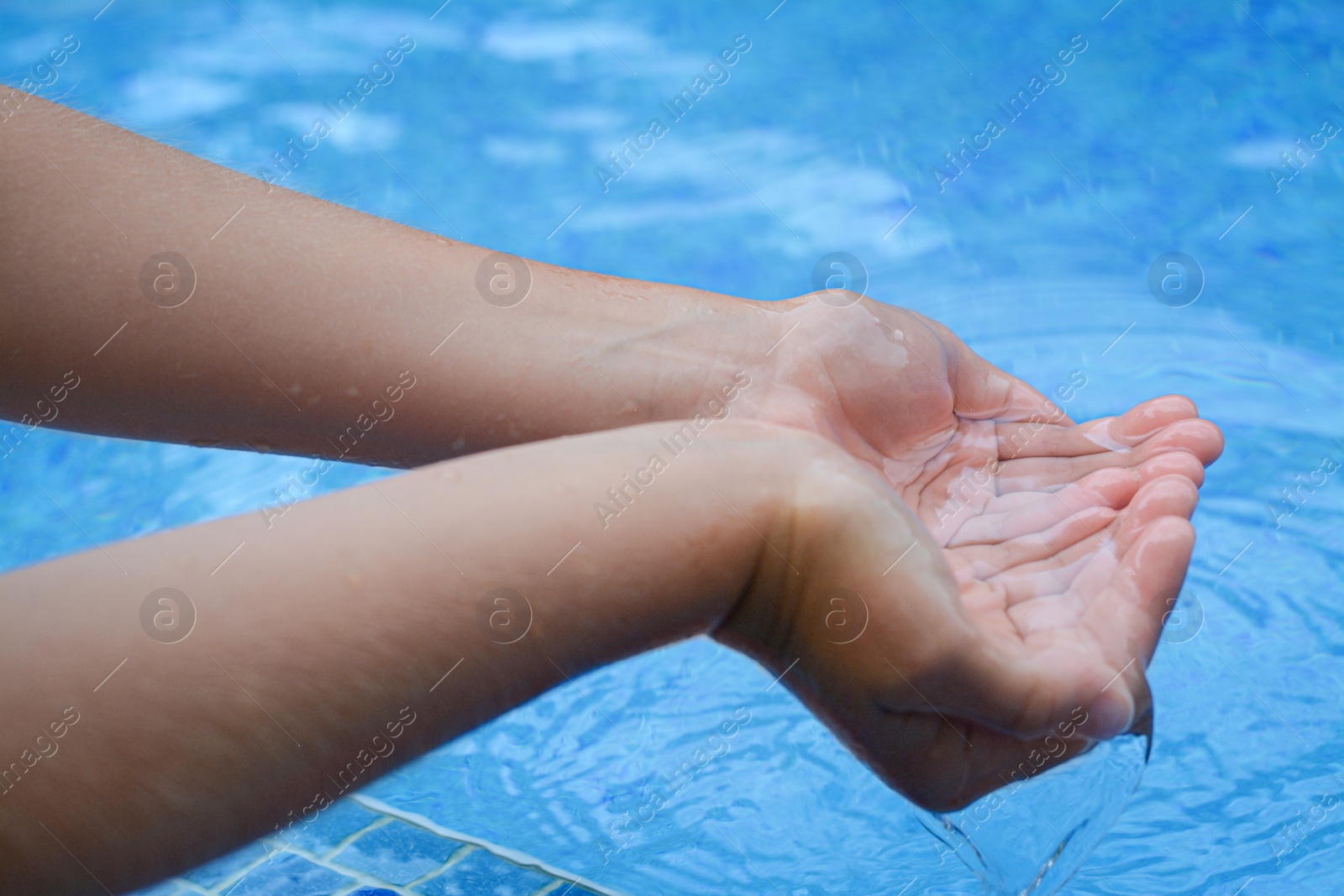 Photo of Girl holding water in hands above pool, closeup