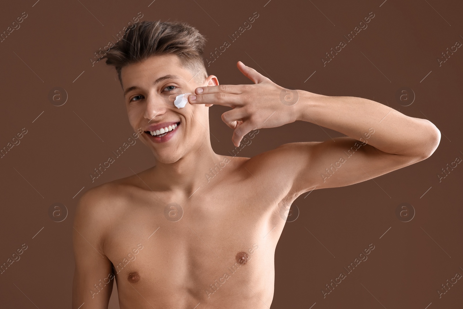 Photo of Handsome man applying moisturizing cream onto his face on brown background