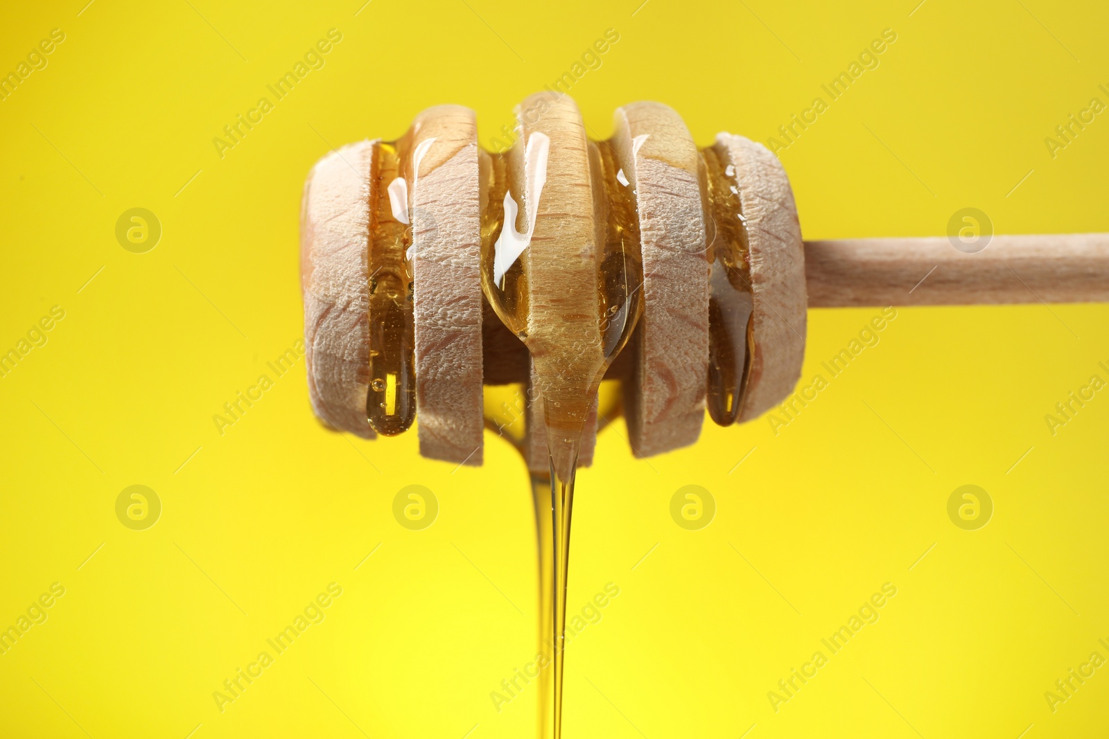 Photo of Delicious honey flowing down from dipper against yellow background, closeup