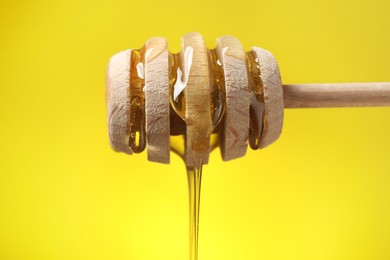 Delicious honey flowing down from dipper against yellow background, closeup