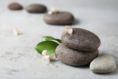 Photo of Spa stones with flowers and leaves on grey table. Space for text