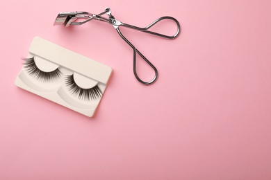 Flat lay composition of curler and false eyelashes on color background, space for text