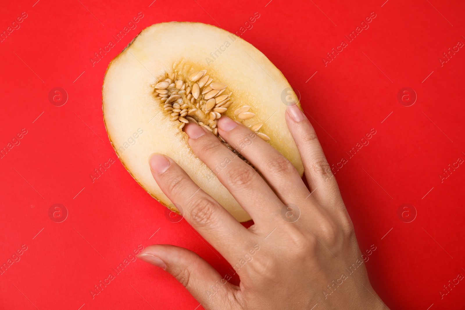 Photo of Young woman touching half of melon on red background, top view. Sex concept