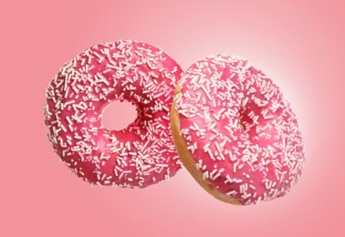 Sweet delicious donuts falling on pink background