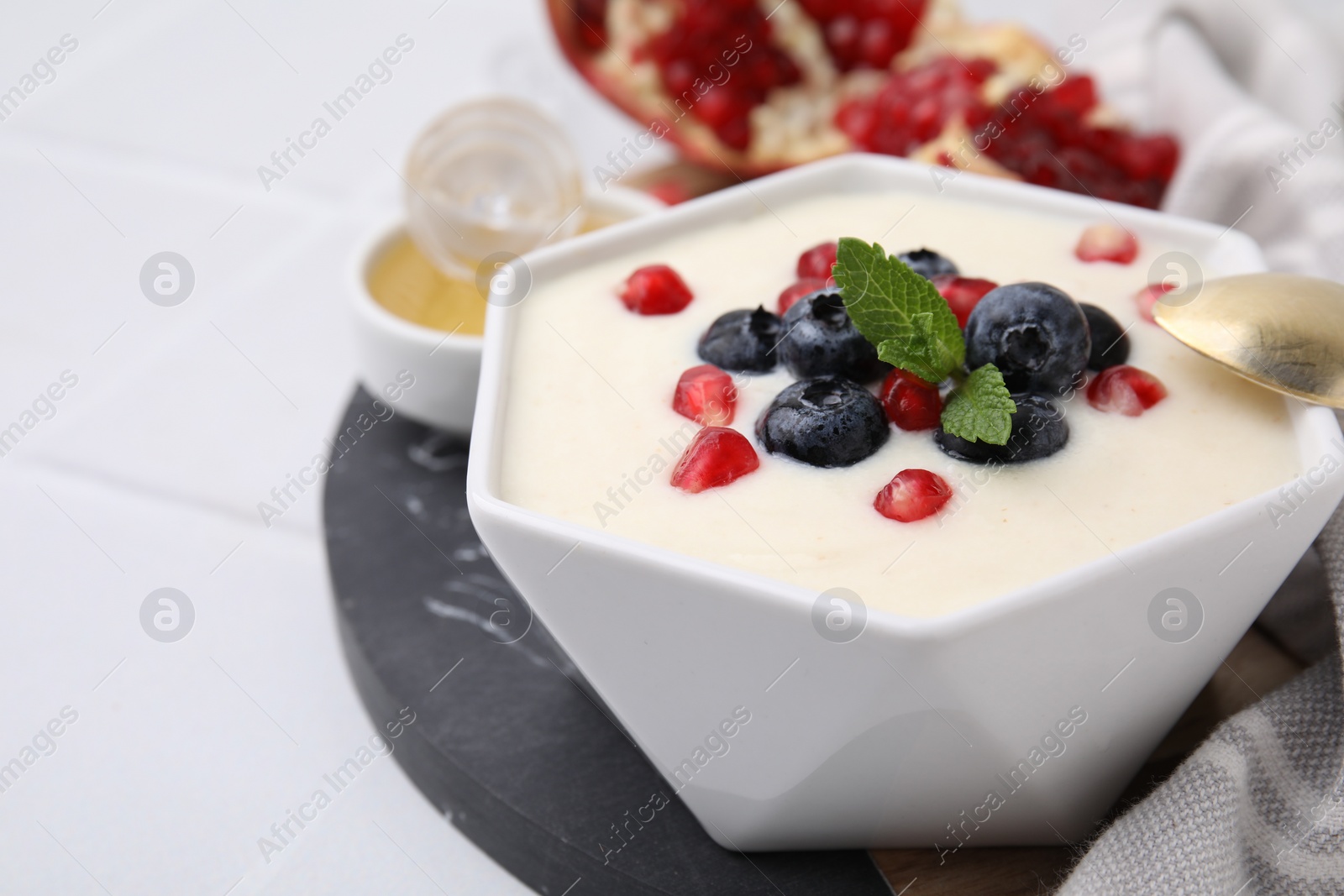 Photo of Bowl of delicious semolina pudding with blueberries, pomegranate and mint served on table, closeup. Space for text