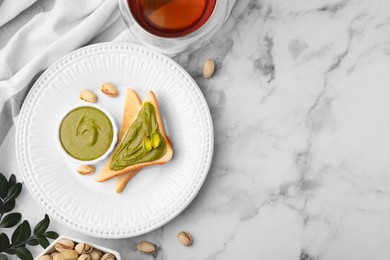 Photo of Tasty pistachio cream in bowl, nuts and toasts on white marble table, flat lay. Space for text
