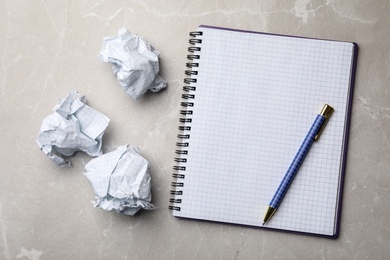 Empty notebook with pen and crumpled paper balls on grey marble table, flat lay. Space for text