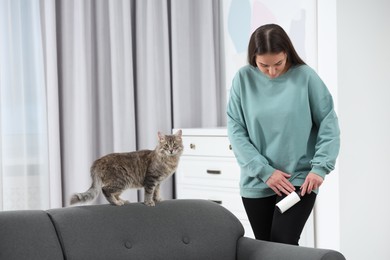 Photo of Pet shedding. Woman with lint roller removing cat`s hair from trousers at home