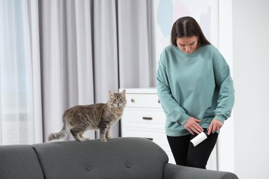 Pet shedding. Woman with lint roller removing cat`s hair from trousers at home