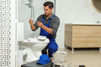 Professional plumber working with toilet bowl in bathroom